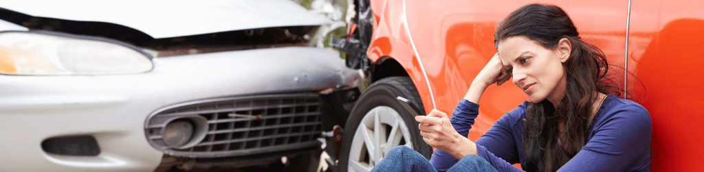 Lady sitting on ground against car door making a distressed phone call after car crash.