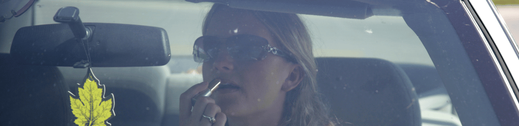 Woman putting on make-up using rearview mirror.