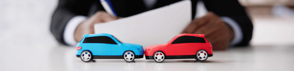 Lawyer filing paperwork at desk; on desk are two toy cars in an accident.