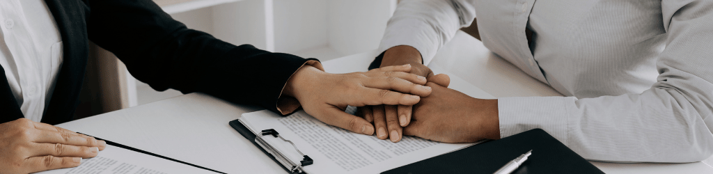 A woman placing a comforting hand upon a mans hands on a table.