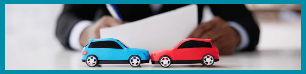 Lawyer filing paperwork at desk; on desk are two toy cars in an accident.