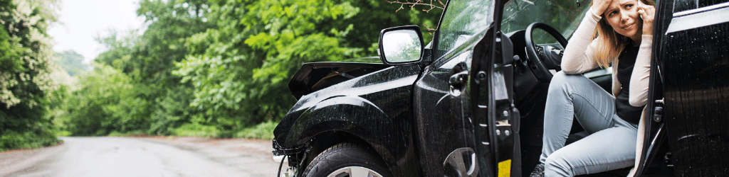 Woman sitting in driver seat, door open, making a distressed phone call after an car accident.